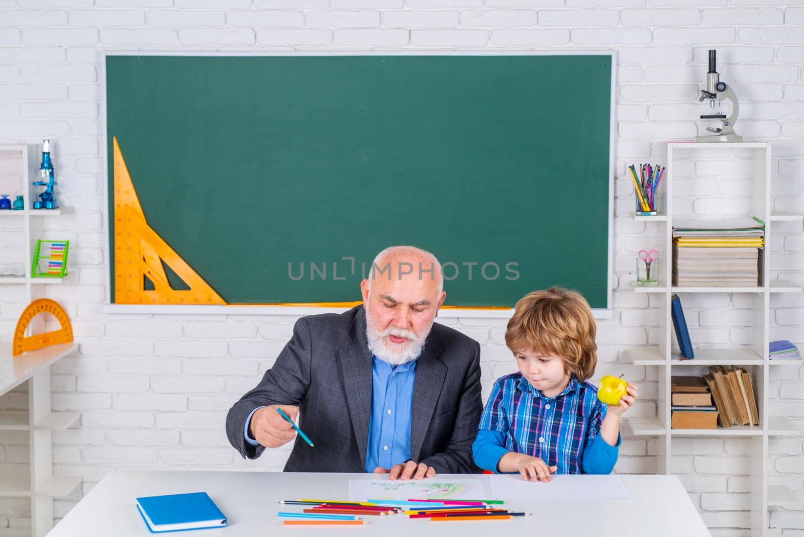 Grandfather with Son learning together. Portrait of confident old male teacher. Concept of a retirement age. A grandfather and a son are learning in class. by Tverdokhlib