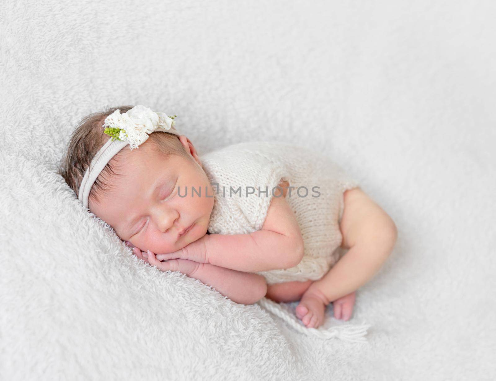 Lovely sleeping baby with a white hairband, dressed in white cute suit napping