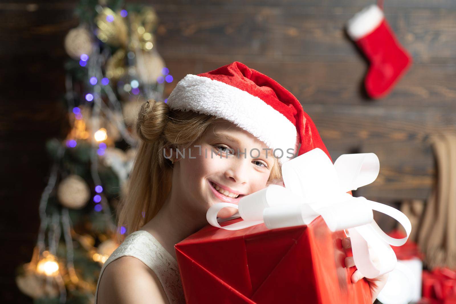 The morning before Xmas. Portrait kid with gift on wooden background. Cute little girl is decorating the Christmas tree indoors
