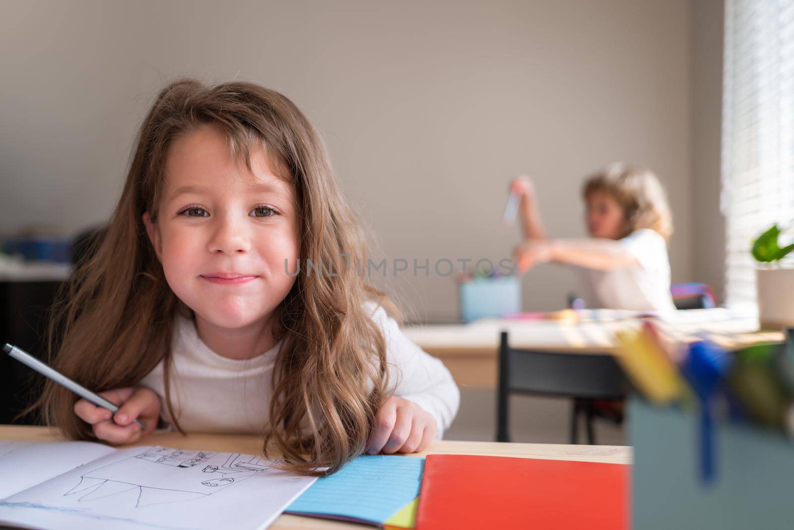 Funny happy schoolgirl writing notes in class. Kids in classroom at school. Pupil at desk in elementary school looking to camera