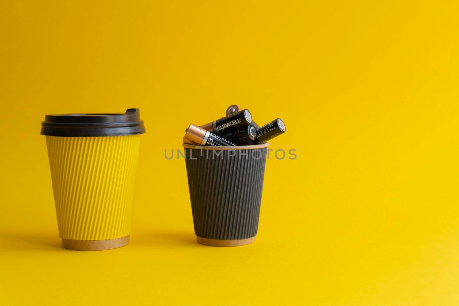 Kiev,Urkaine,16 June 2020,Two takeaway paper coffee cups,yellow with coffee and plastic cover,black cup with Duracell AA batteries,association of energy,yellow background,creative idea,space for text.