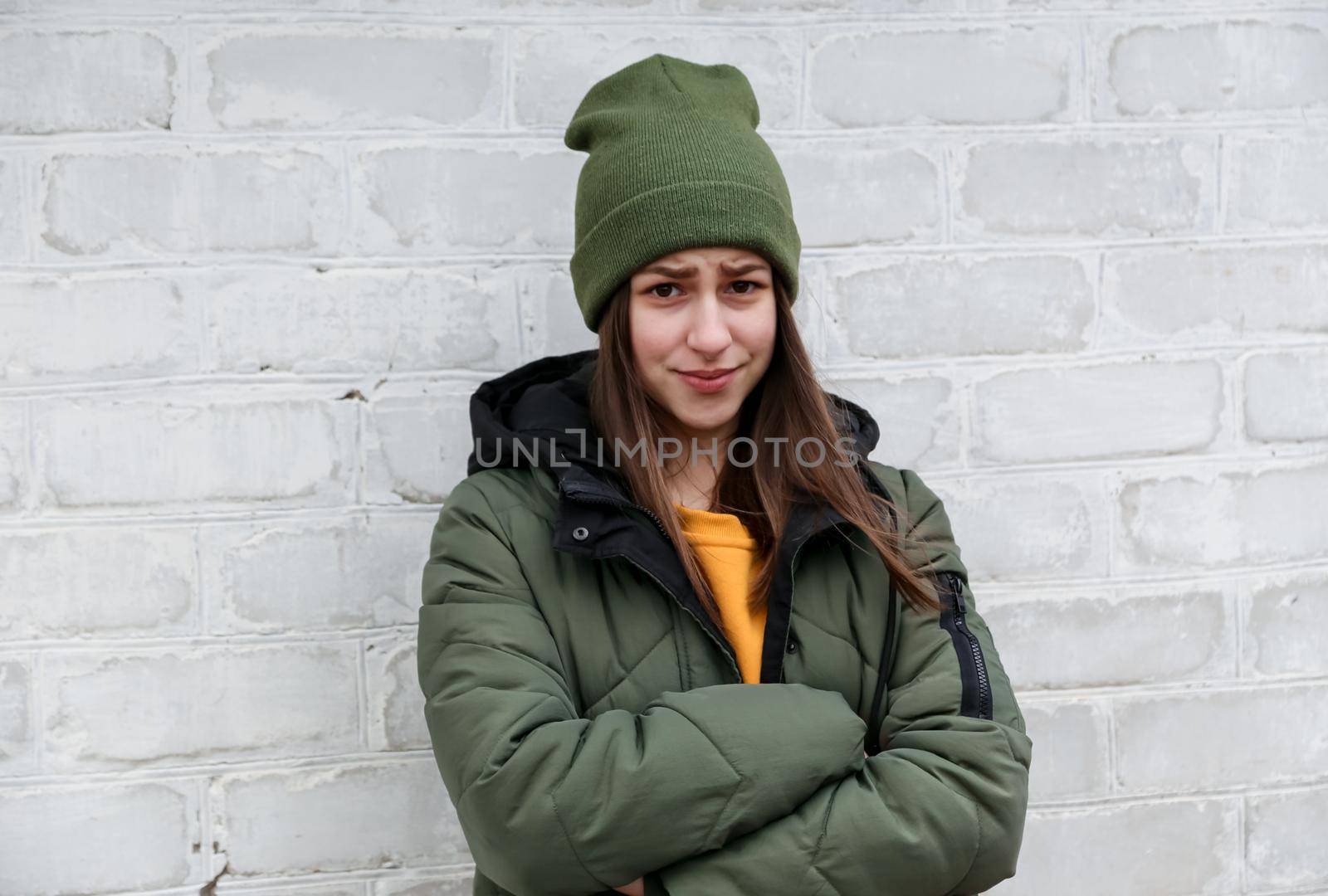 Portrait of a beautiful shy girl in a yellow sweater and khaki hat, which stands near a white brick wall. The concept of emotions and copy space by lunarts