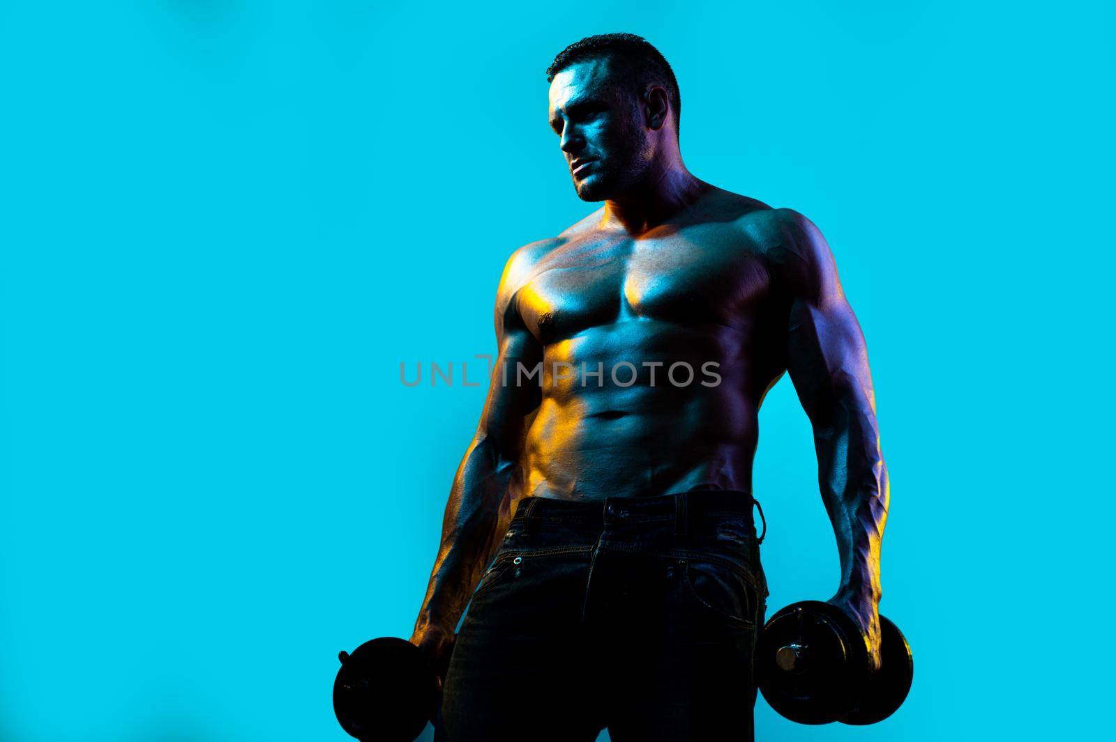 Exercise for the muscles biceps. Muscular bodybuilder guy doing exercises with dumbbells isolated on blue neon. by Tverdokhlib