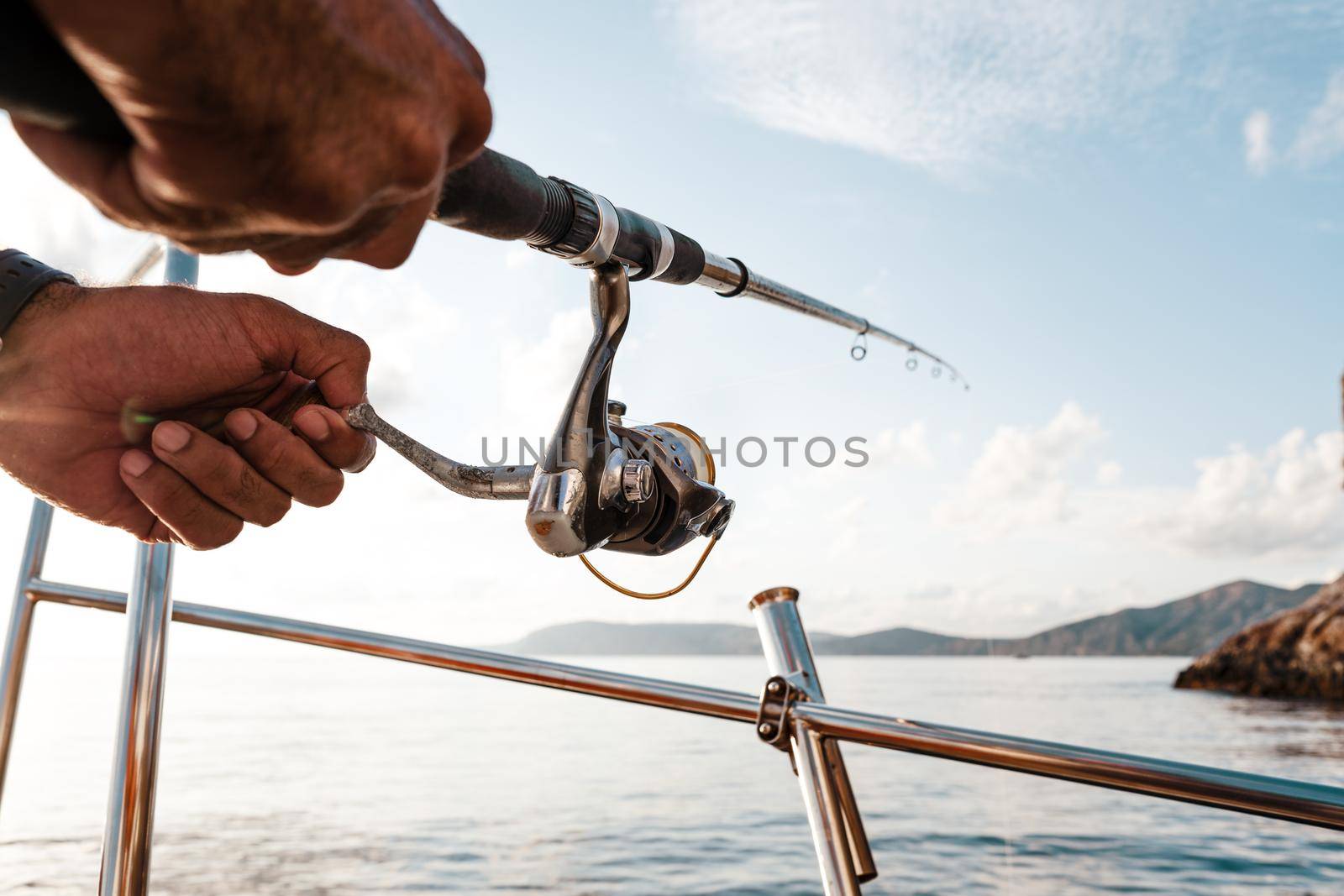 Close up of male hands holding fishing rod while fishing on sailboat in open sea by Fabrikasimf