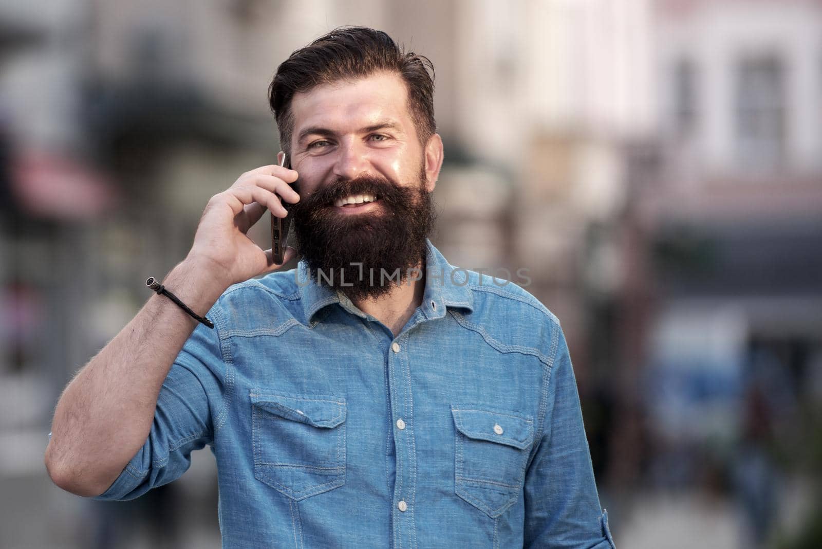 Smiling man call phone and smile outdoor city street. Happy businessman in casual blue shirt talking on mobile