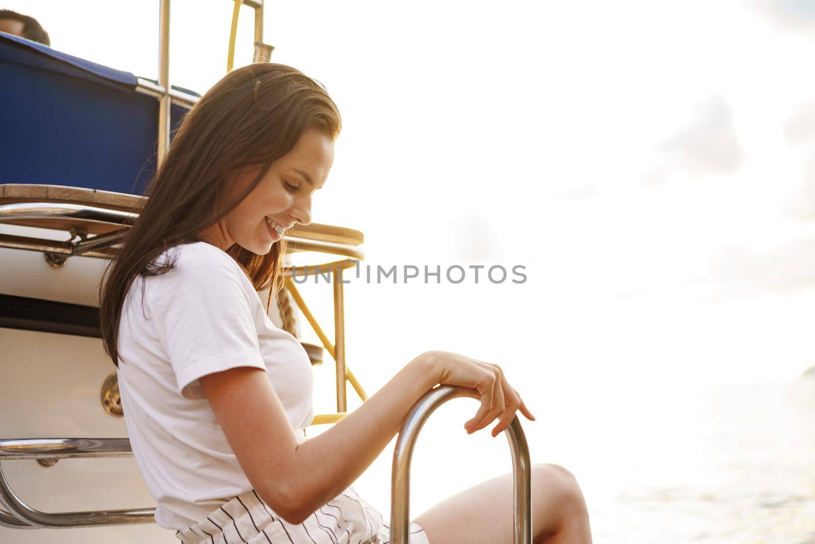 Girl sits on the edge of the yacht with legs splashing in sea water by Fabrikasimf
