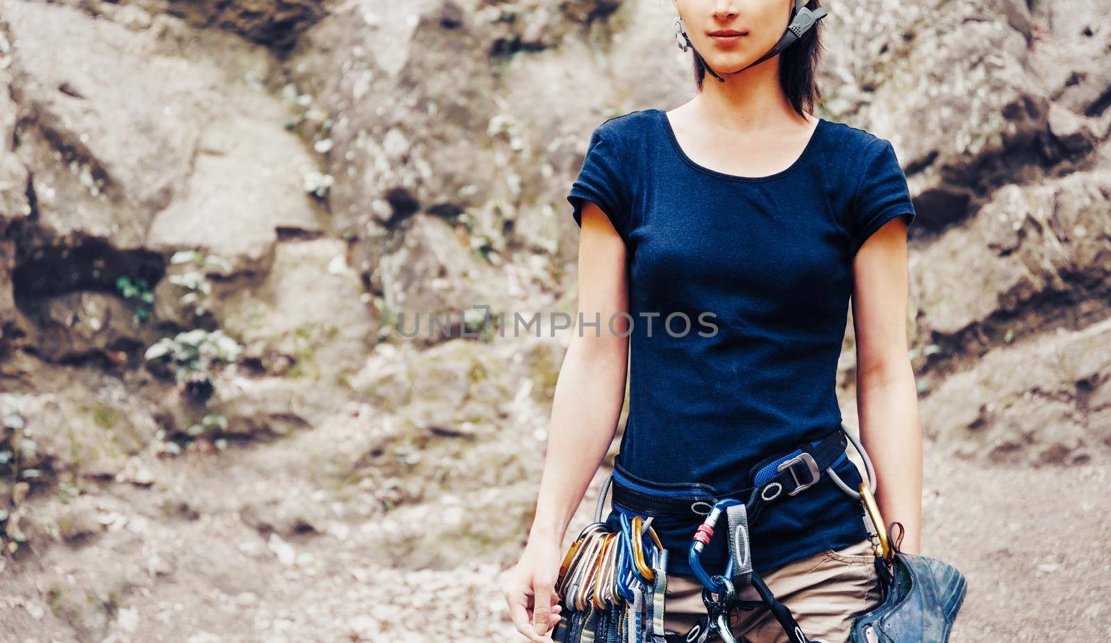 Young woman with climbing equipment standing in front of rock and preparing to climb.