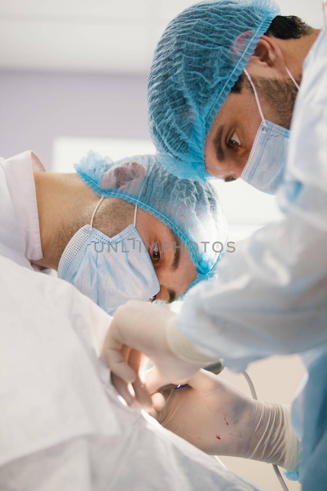 Two surgeons in blue robes make operation in surgery room by Studia72