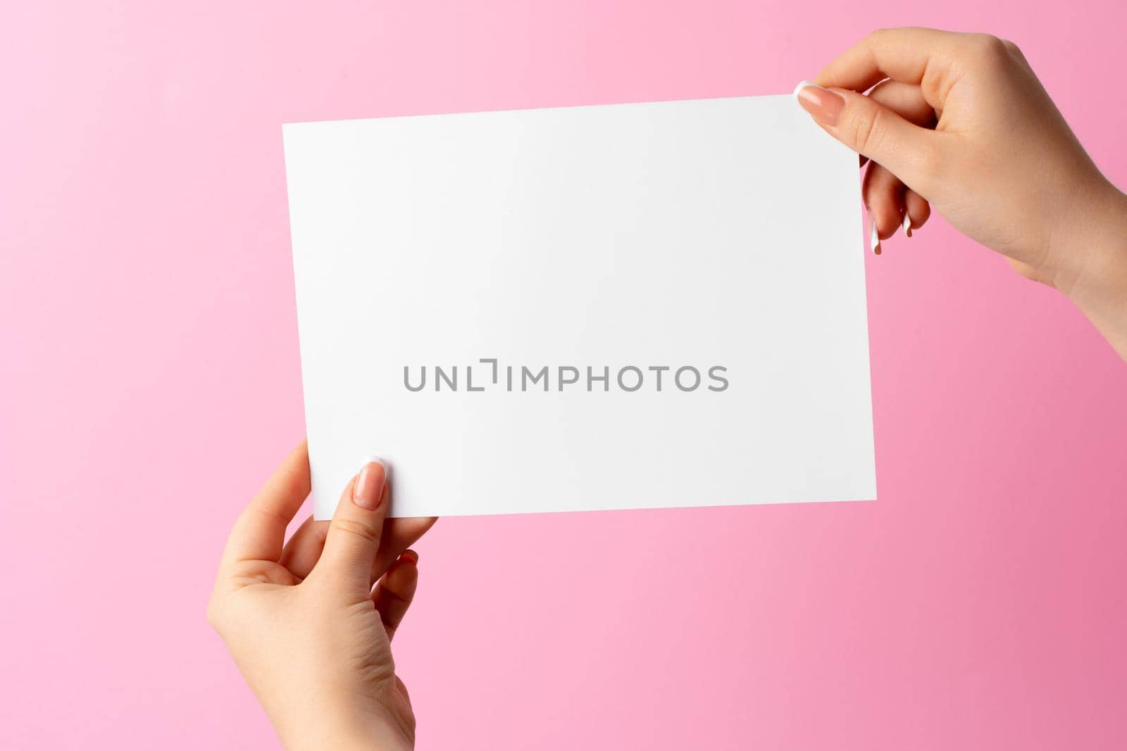 Woman hand showing blank business card on pink background. Close up.