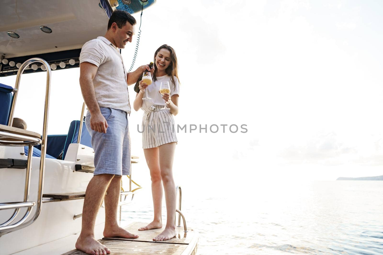 Young loving couple sitting on the yacht deck and drinking wine together