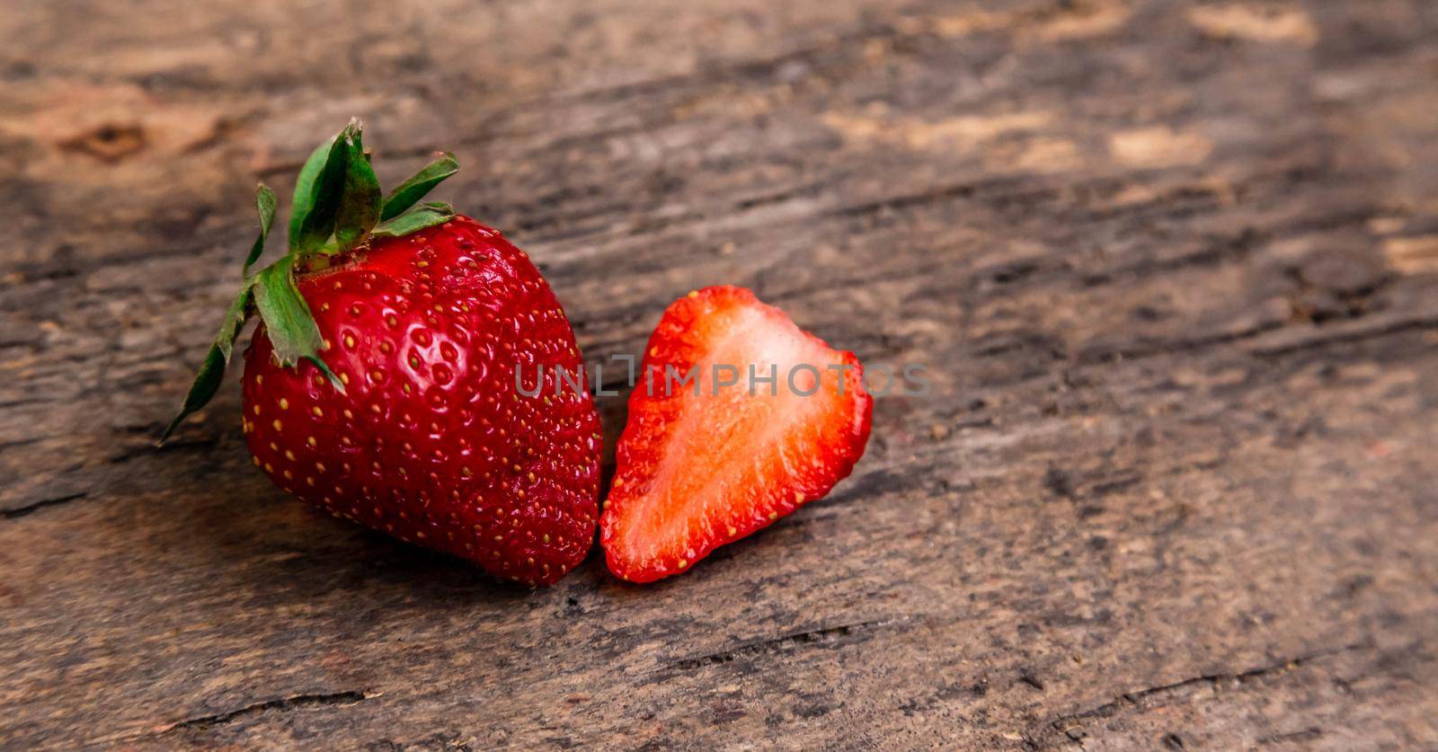 One whole strawberry and one half strawberry on a dark wooden surface with space to write on the right.