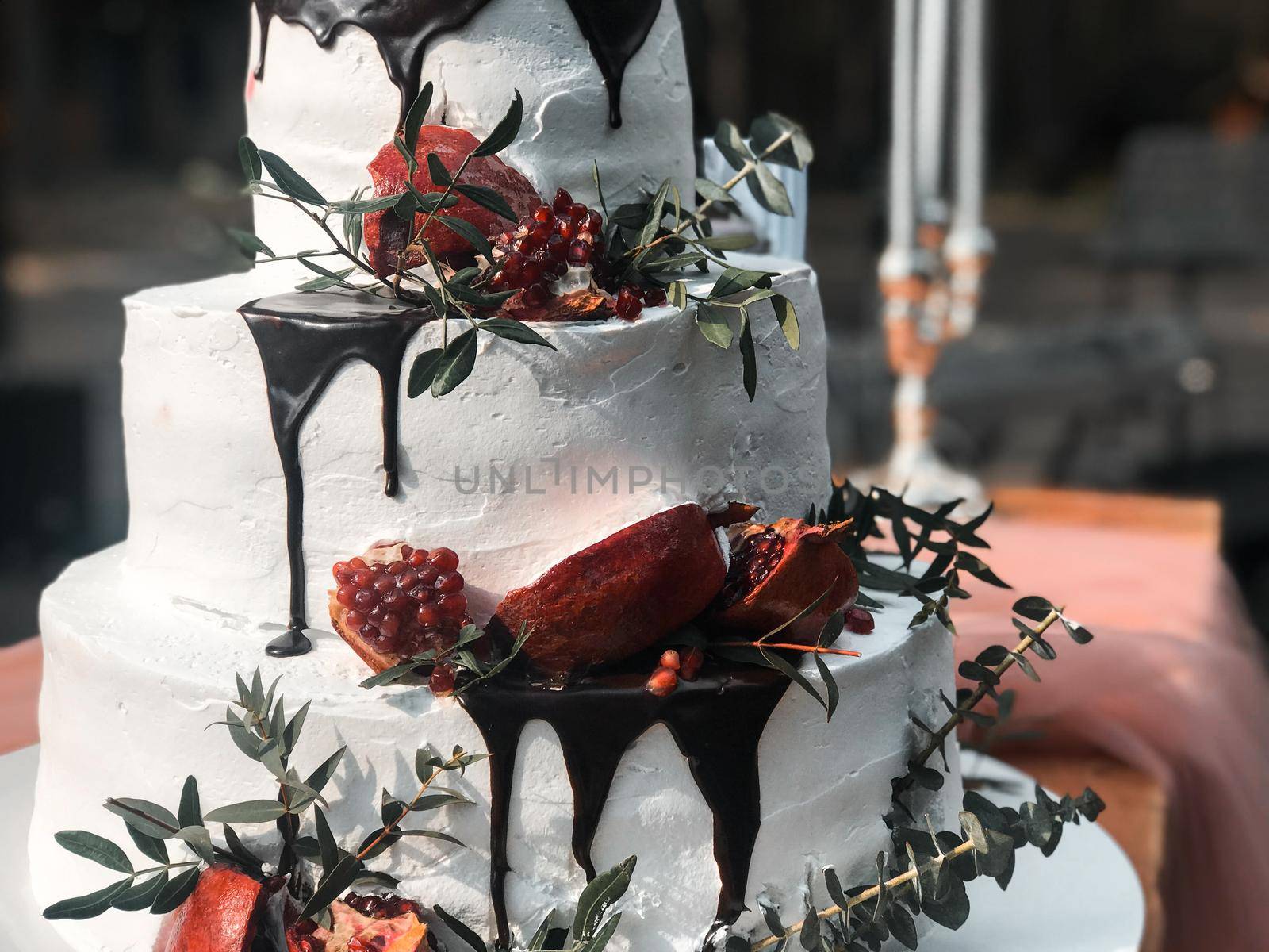 Beautiful three-tiered white cream wedding cake with pomegranate fruit and fresh flowers.