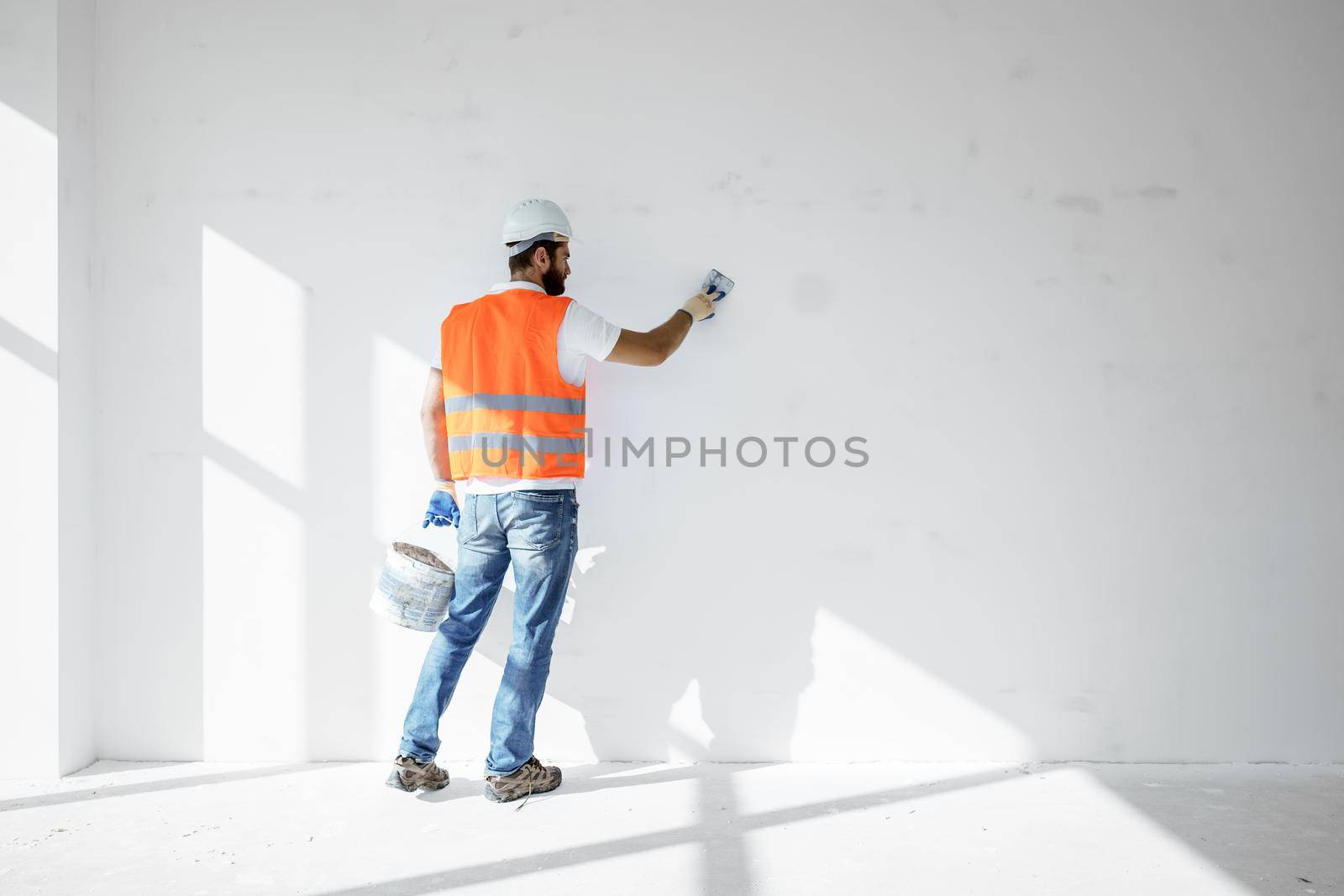Plasterer in workwear smoothing wall surface of building indoors by Fabrikasimf