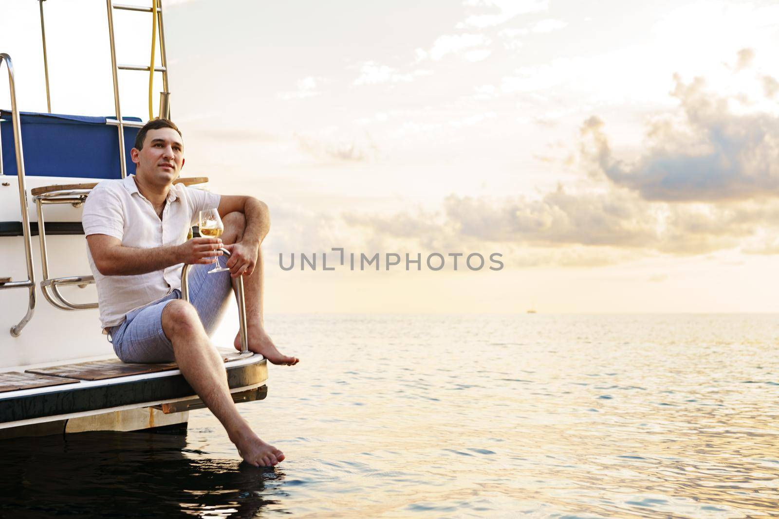 Young man holding a glass of wine on an open deck of a cruise boat, close up