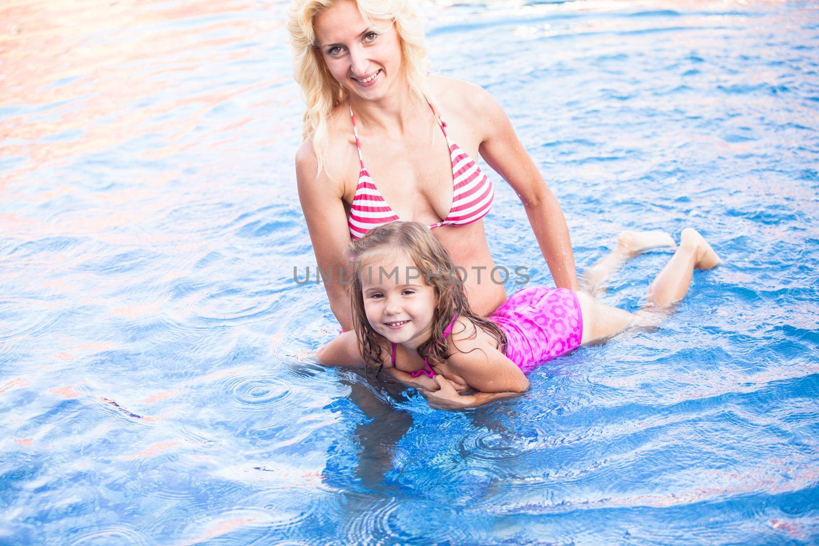Mother is teaching her daughter to swim at the swimming pool