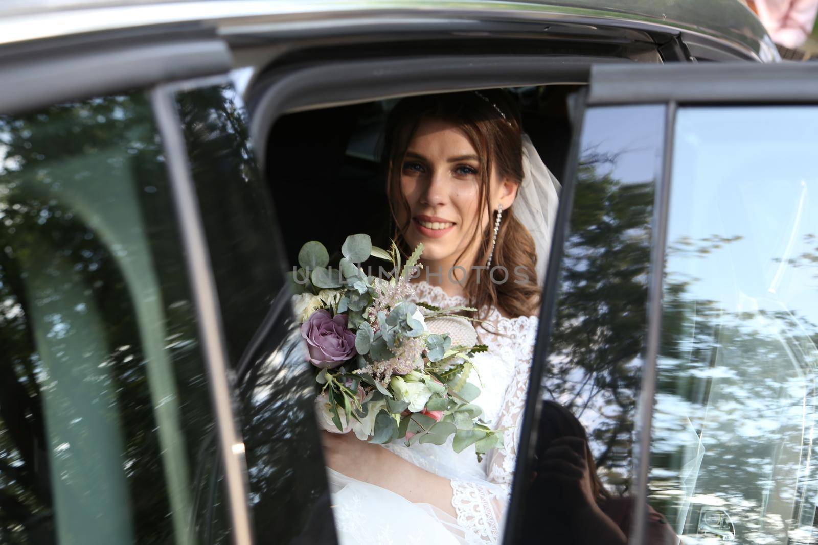 Wedding photo of the bride who is sitting in the car with a bouquet of flowers. by lunarts