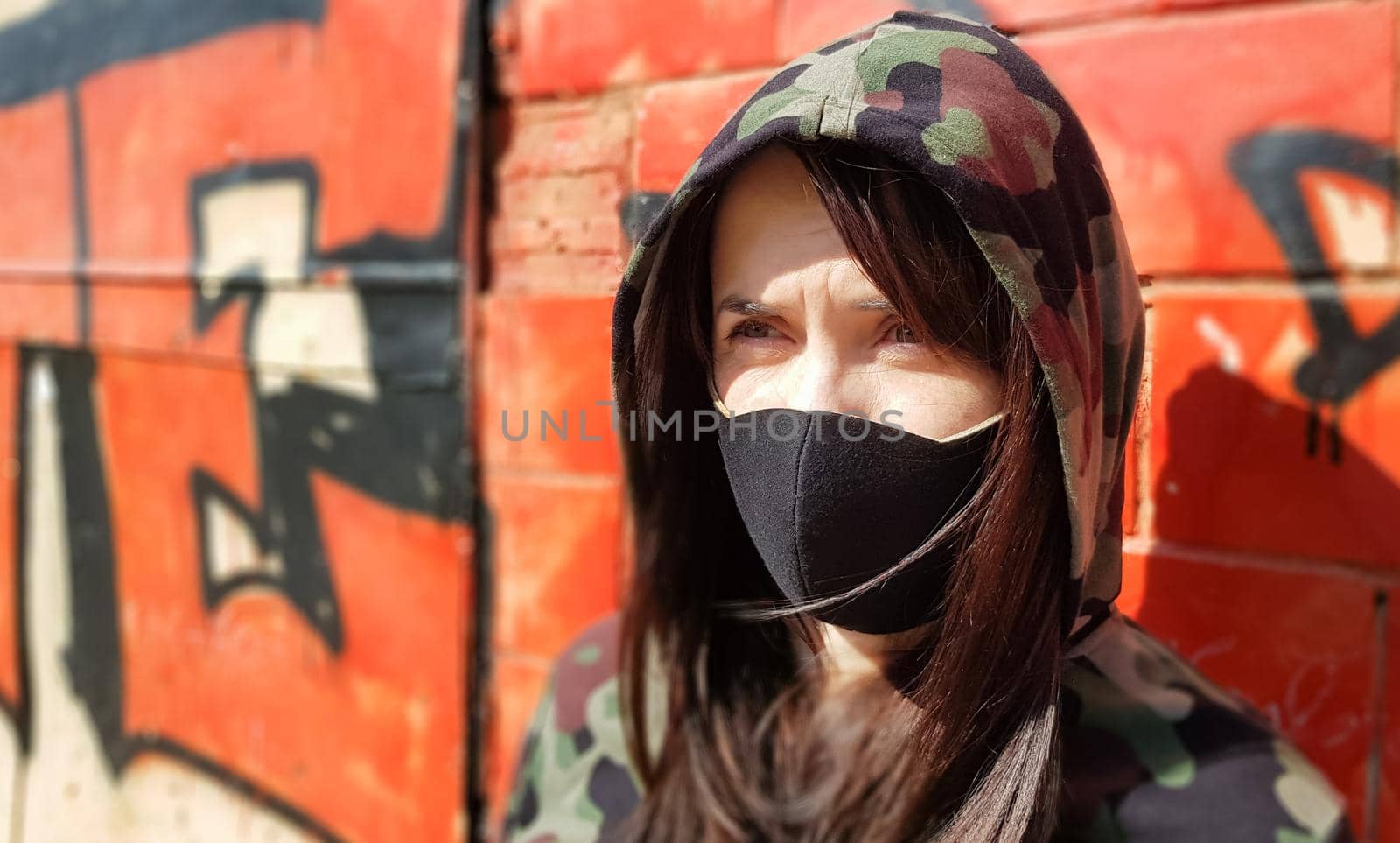 Portrait of a woman in a protective black mask outdoors near an old broken wall. Coronavirus and air pollution concept. A girl wears a protective mask to protect against a pandemic
