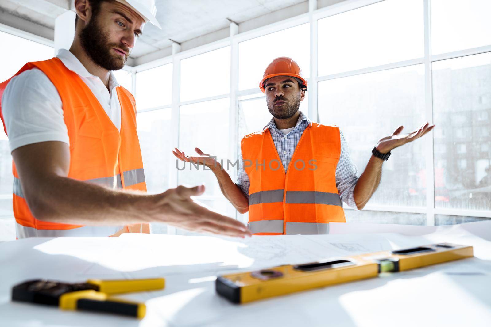 Two young engineers man looking at project plan on the table in construction site