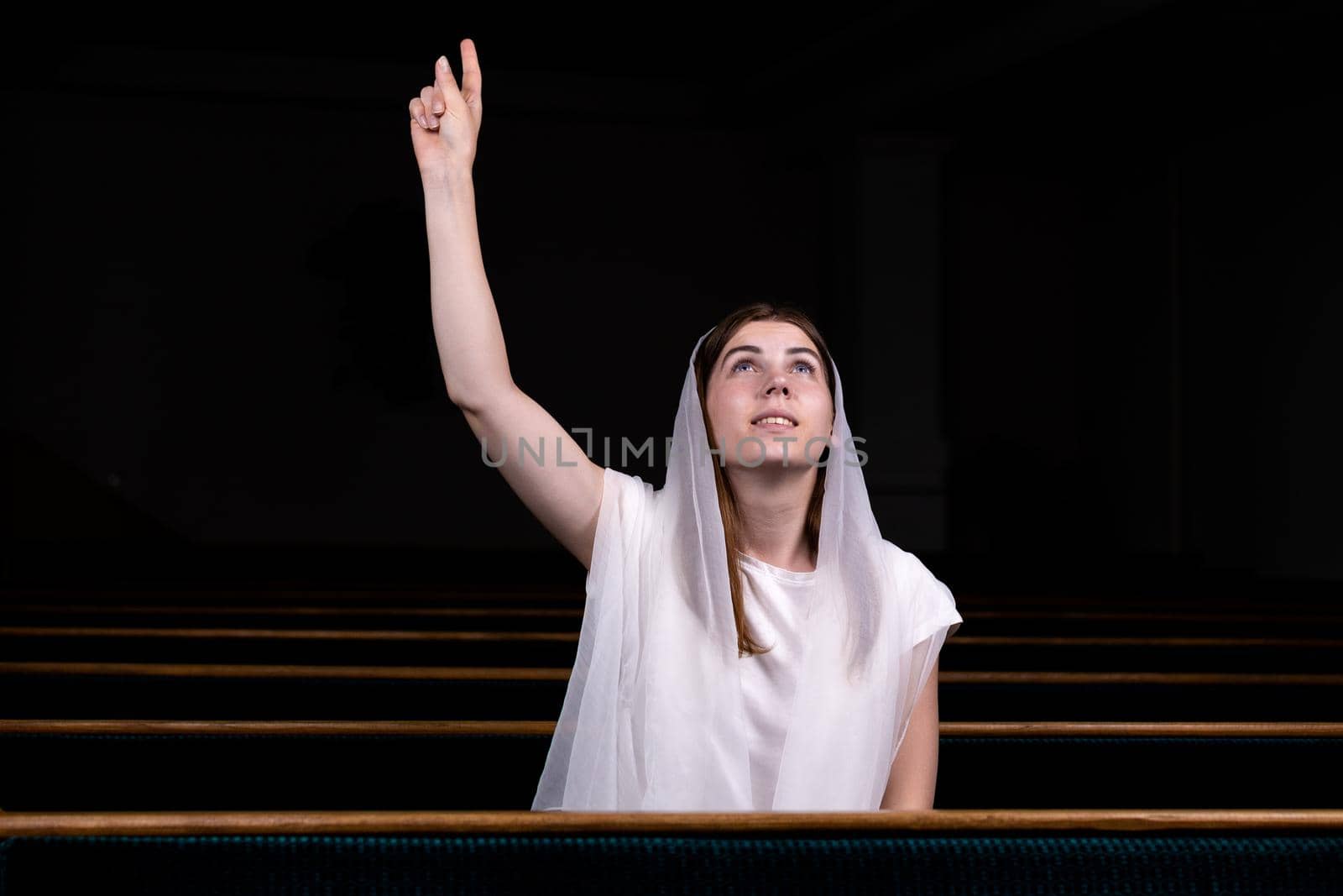 A young modest girl with a handkerchief on her head is sitting in church and praying. The concept of religion, prayer, worship.