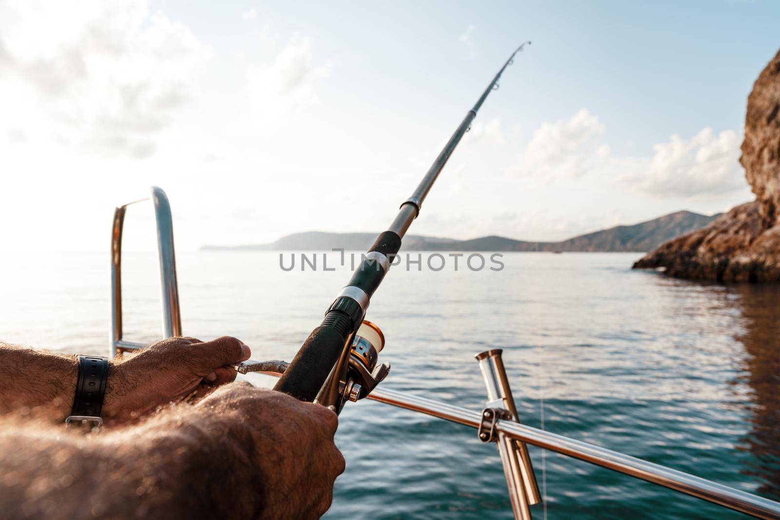 Close up photo of male hands holding fishing rod while fishing on sailboat in open sea