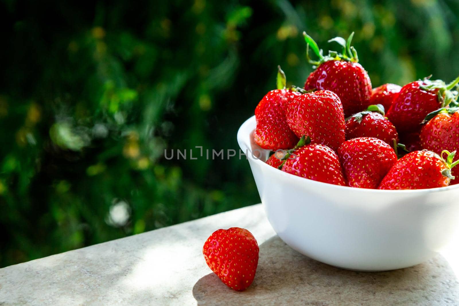 Red ripe strawberry in the white bowl, green background