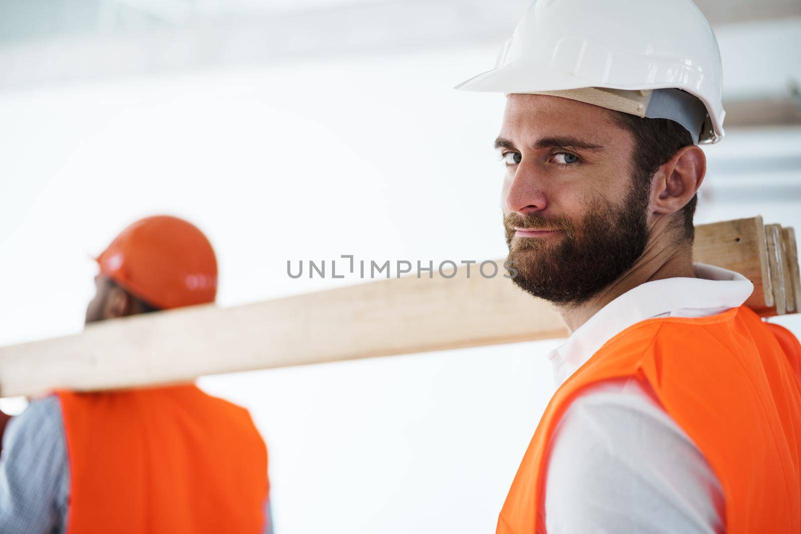 Two young men builders carrying wood planks on construction site, close up by Fabrikasimf