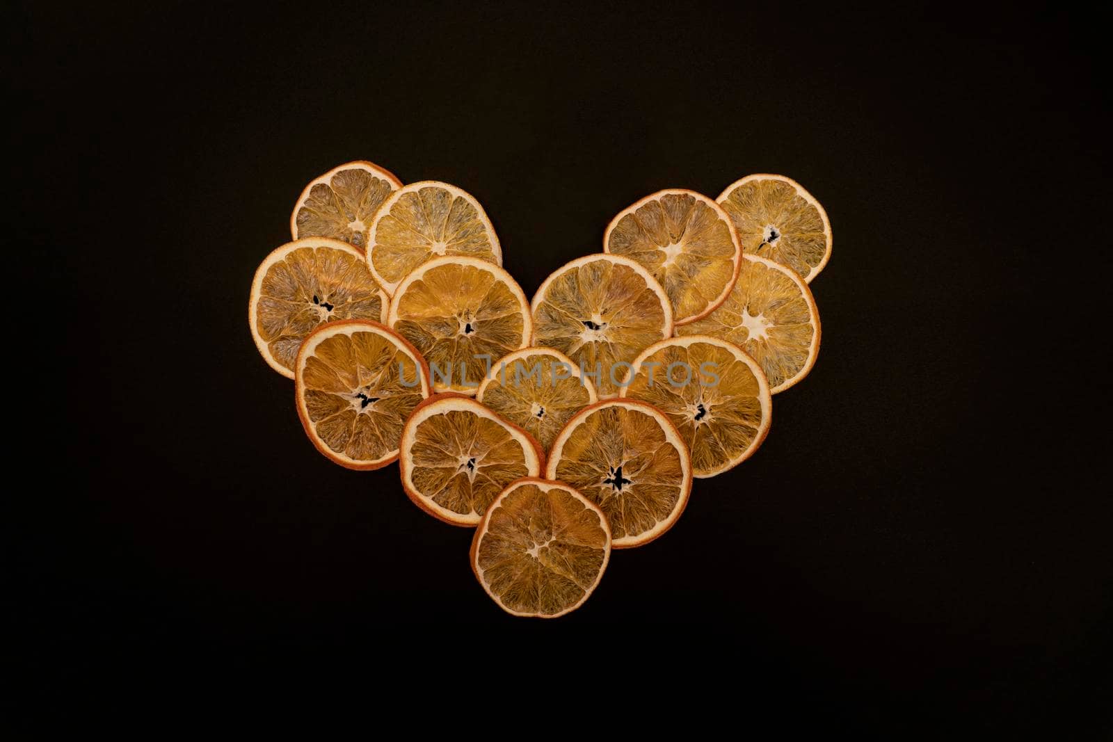 Dried fruit oranges in the shape of heart, symbol of valentine s day, day for lovers, creative concept, full of love, flat lay, black background, copy space.