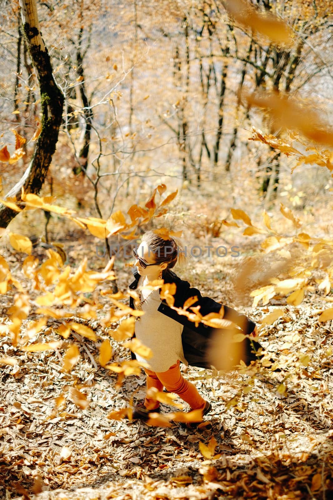 Happy young woman walking in autumn park on fallen leaves among trees.