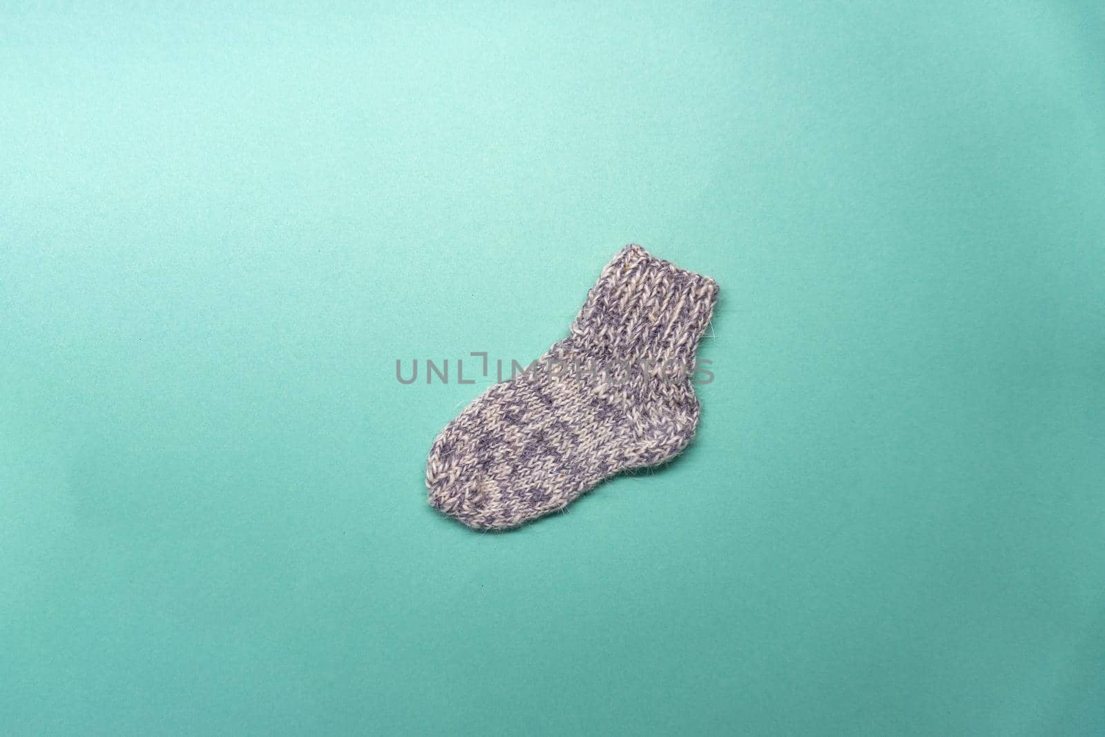 Knitted gray and white sock is on light green background. Flat lay of a handmade work.