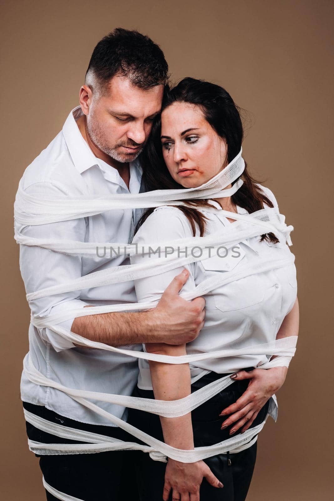 An aggressive man embraces a battered woman and is wrapped in bandages together. Domestic violence by Lobachad