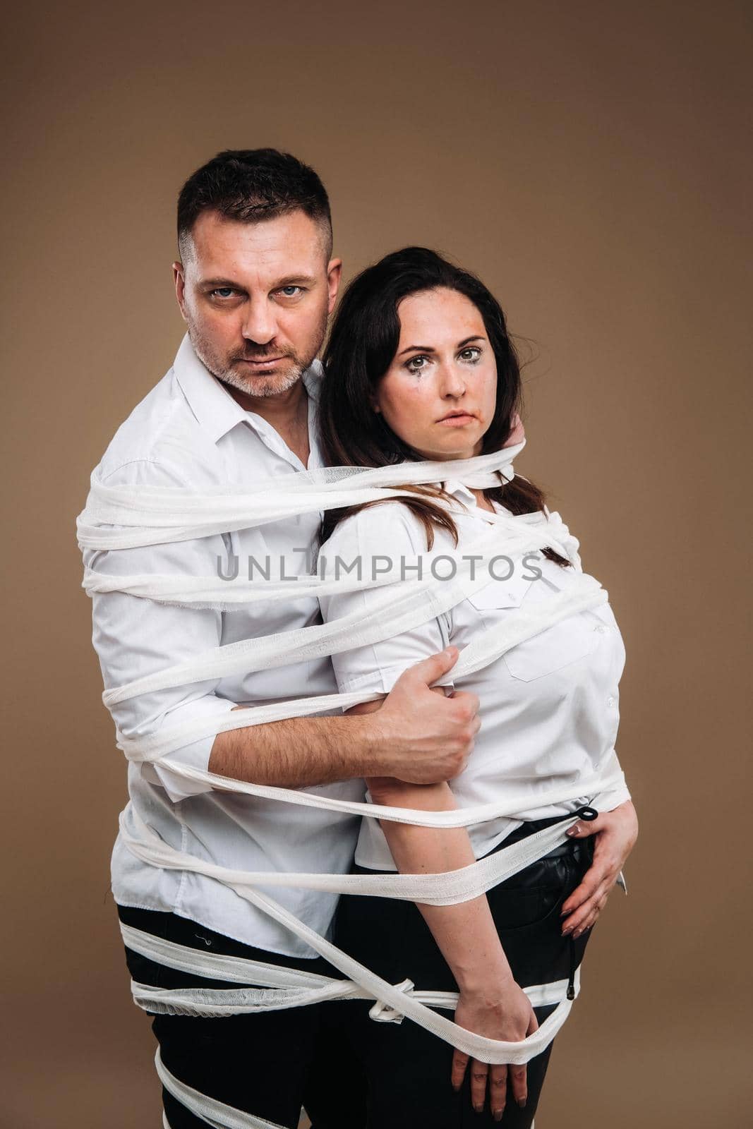 An aggressive man embraces a battered woman and is wrapped in bandages together. Domestic violence by Lobachad