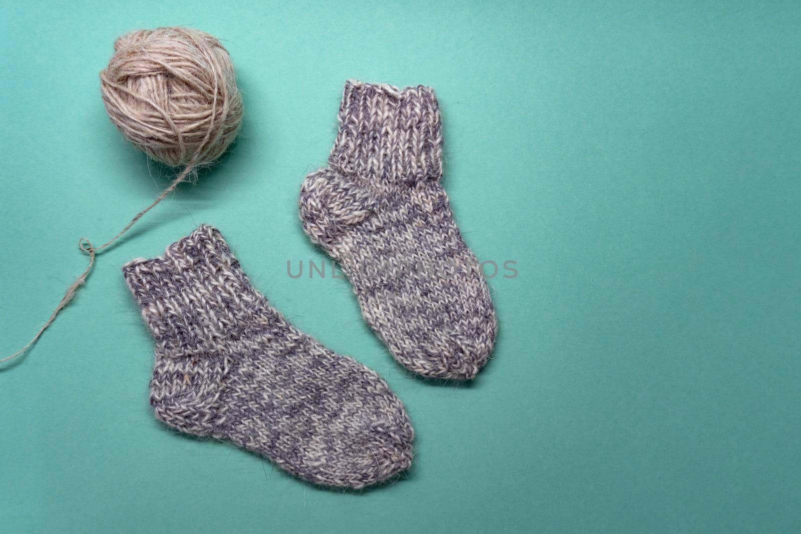 Flat lay of knitted warm winter socks and thread on light green background. View from the top.
