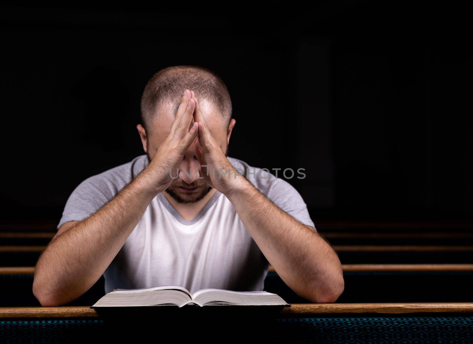 A young guy sits on a church bench, reads the bible and prays. The concept of religion, prayer, faith