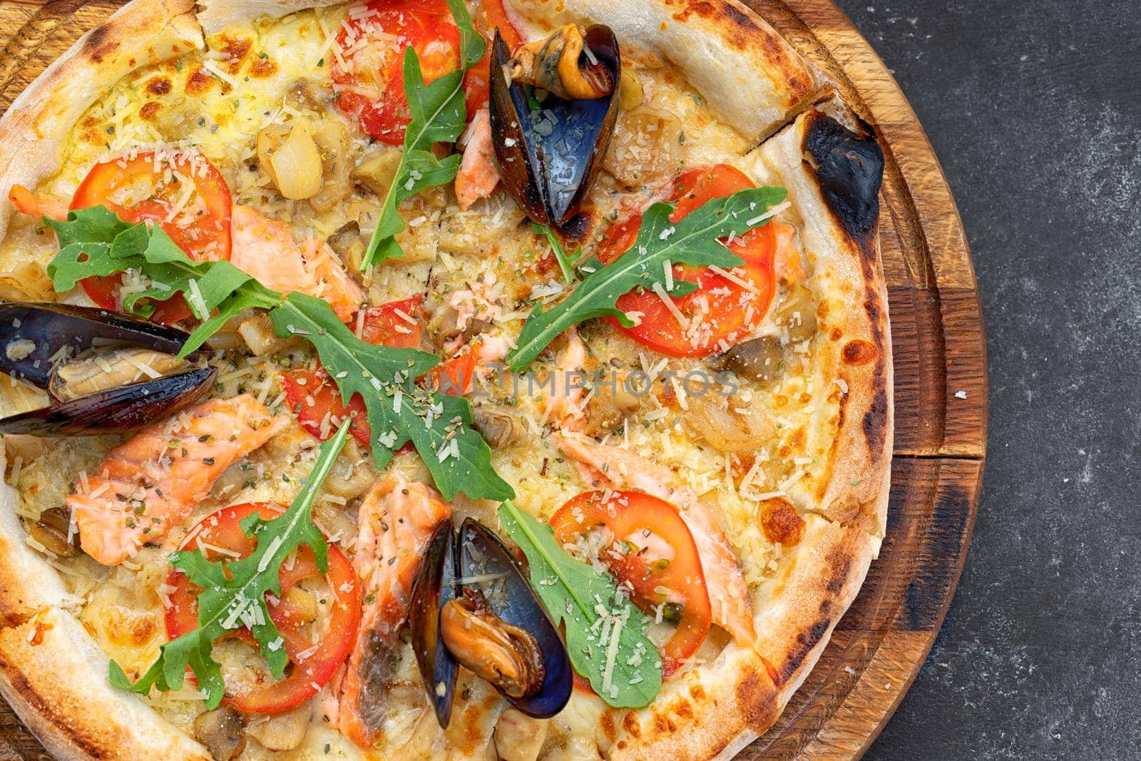 Pizza with seafood mussels shrimp salmon scallop on a wooden board, on a dark background