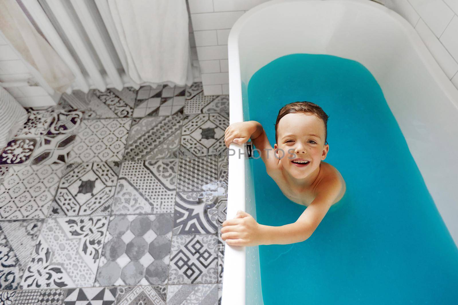 Cute child bathing in blue water in bathtub by Demkat
