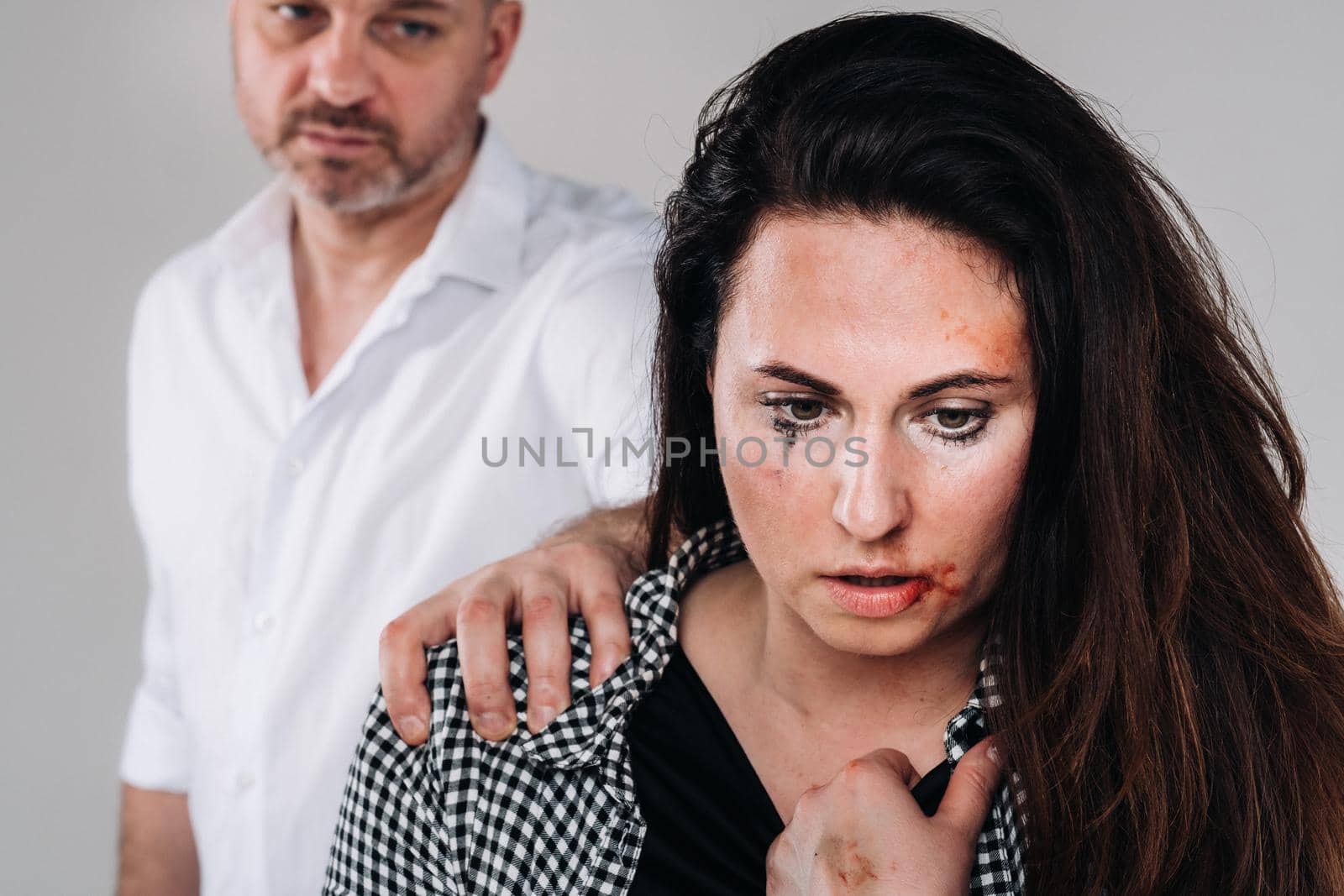 A woman beaten by her husband standing behind her and looking at her aggressively. Domestic violence.