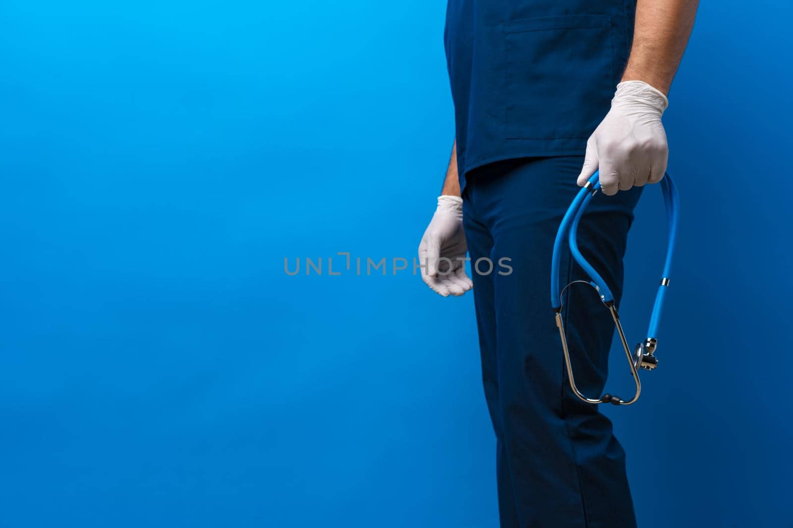 Unrecognizable male doctor holding stethoscope against blue background, close up