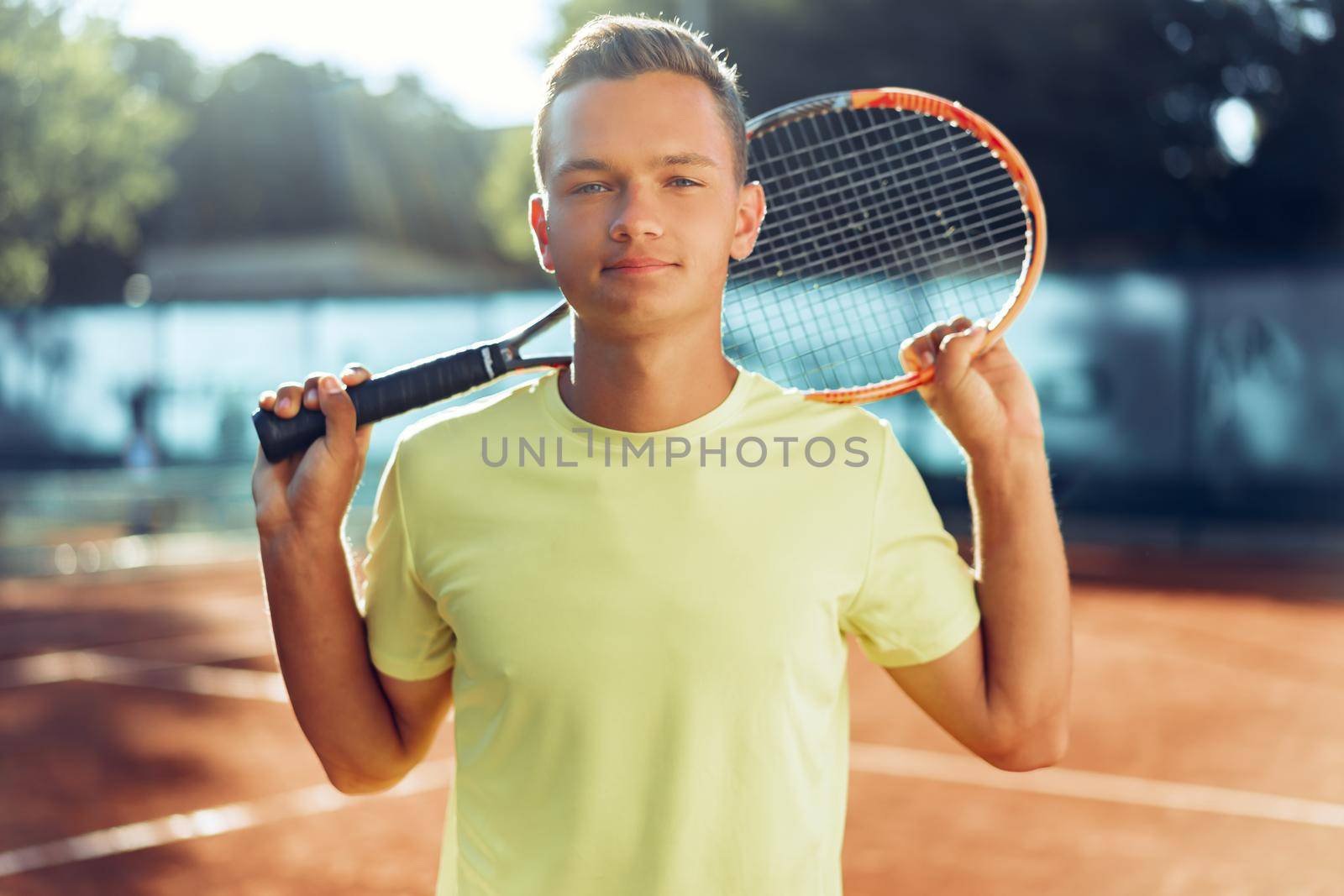 Young man teenager with tennis racket standing near net on clay tennis court