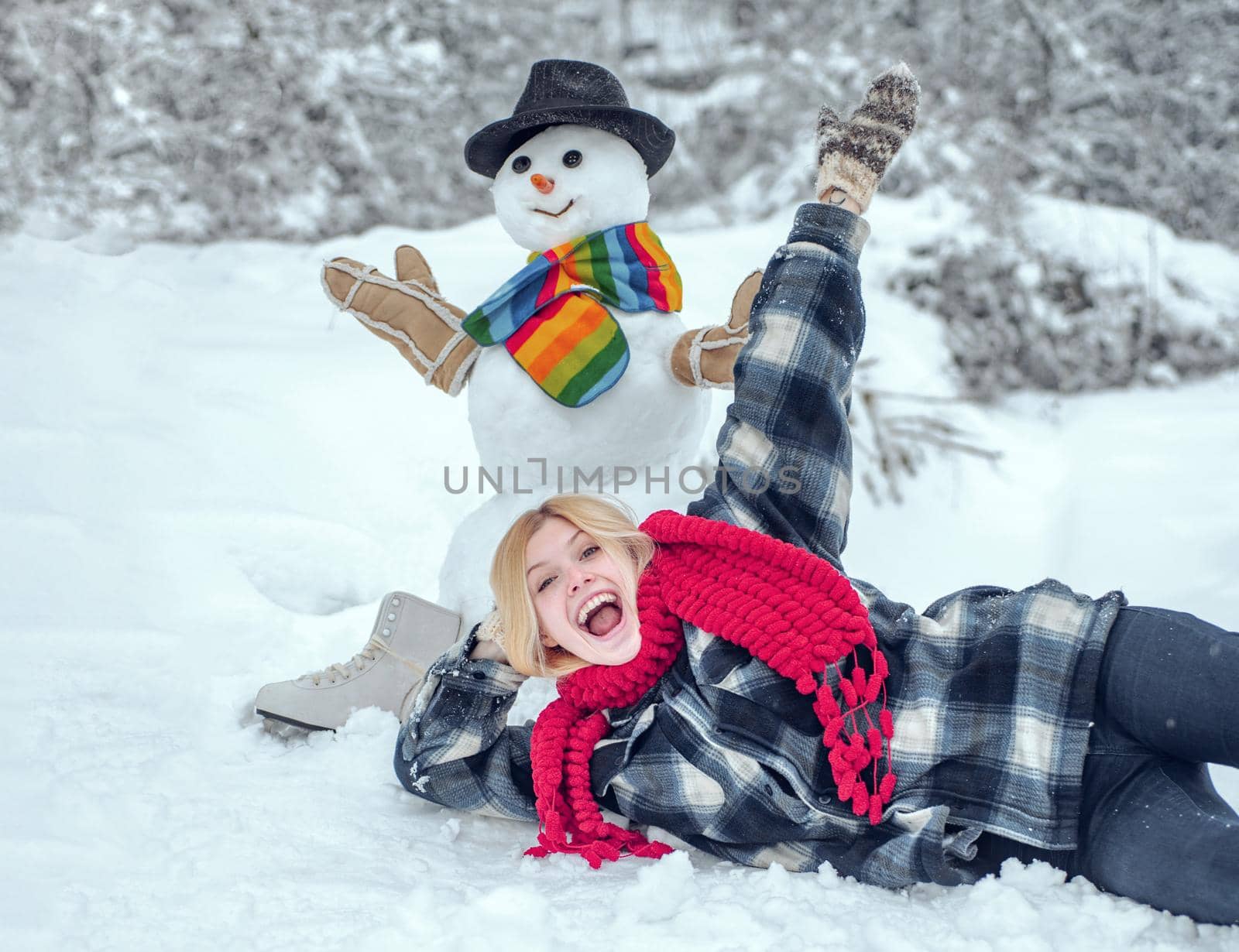 Winter woman. Greeting snowman. Snowman and funny female model standing in winter hat and scarf with red nose. Cute snowman at a snowy village