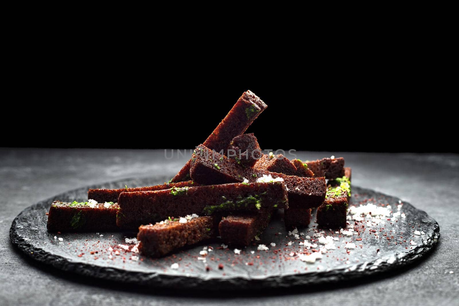 Black bread toast for beer with garlic salt and herbs on a black background