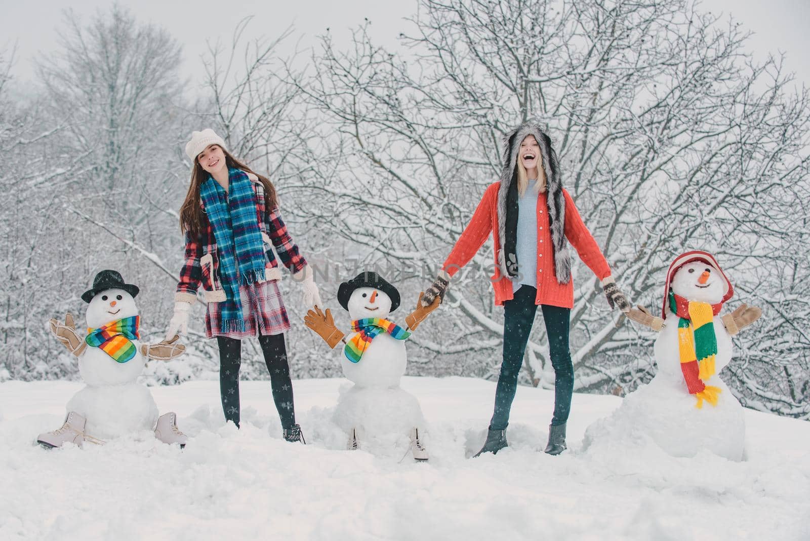 Group of girls with snowman outdoors. Students winter party and Christmas celebration. Two Joyful young women having fun with snowman. Merry Christmas and Happy new year