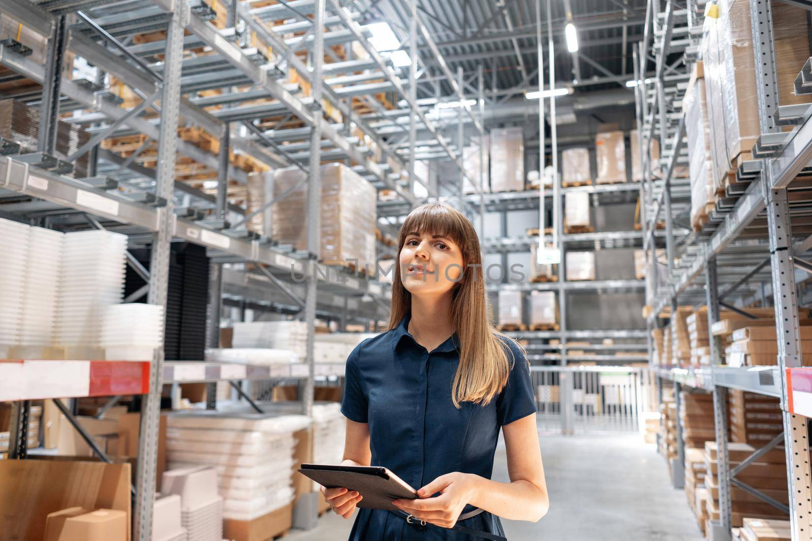 Wholesale warehouse. Beautiful young woman worker of store in shopping center. Girl looking for goods with a tablet is checking inventory levels in a warehouse. Logistics concept.