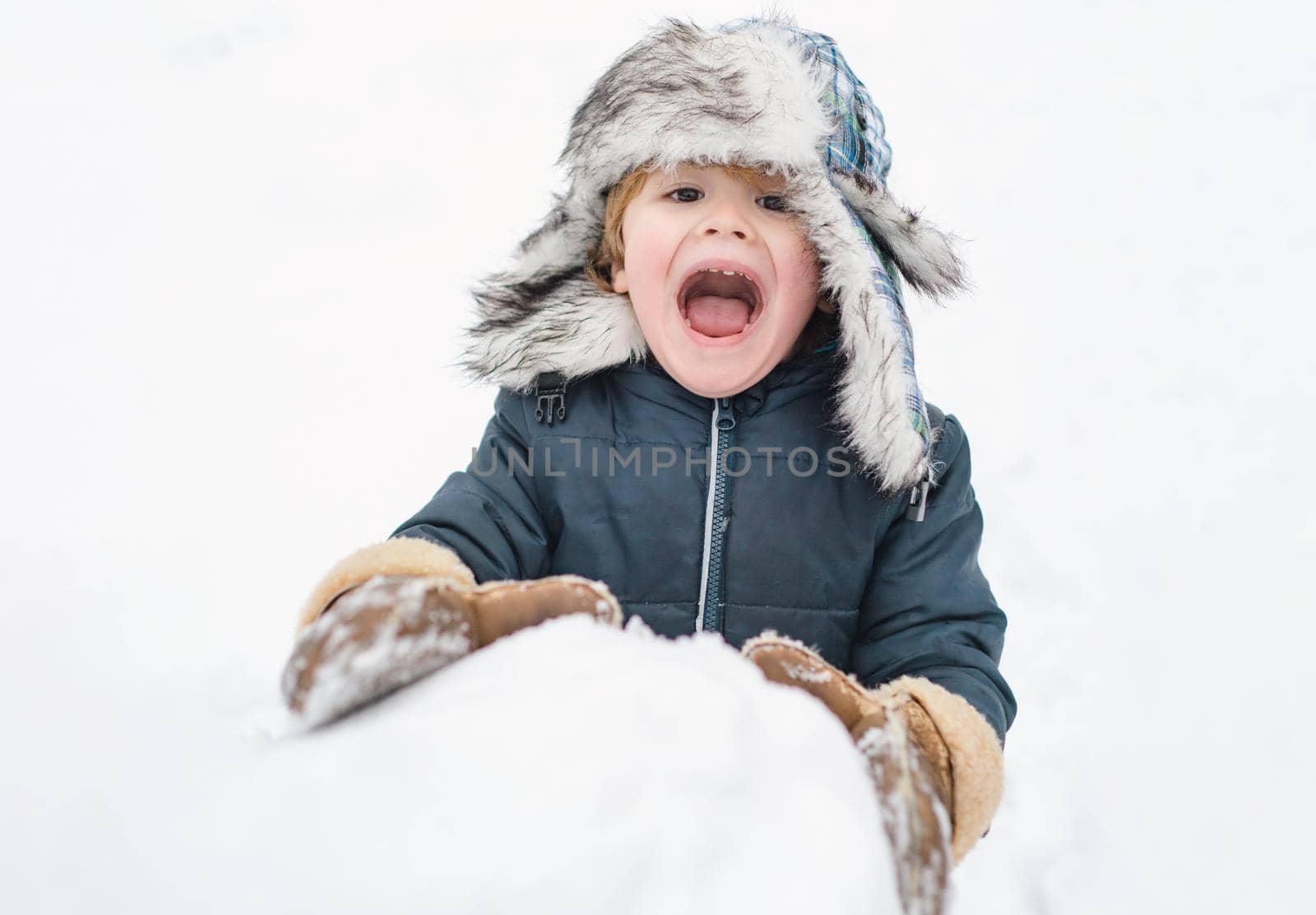 Excited child playing with a snow. Cute child in winter hat having fun with snowball in winter park. Winter clothes for kids