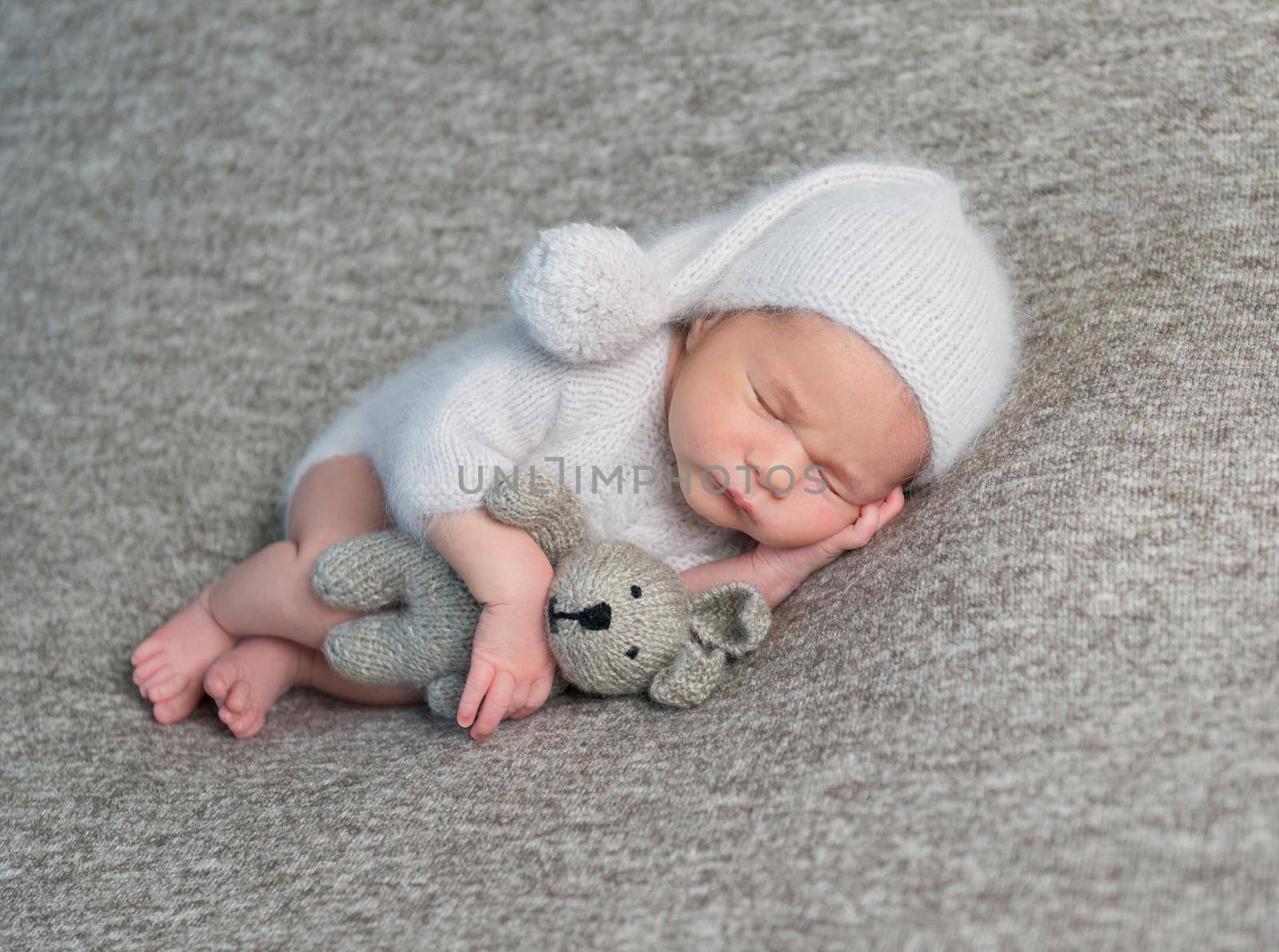 Sweet little baby boy in light blue costume and knitted bonnet with pom pom on grey background.