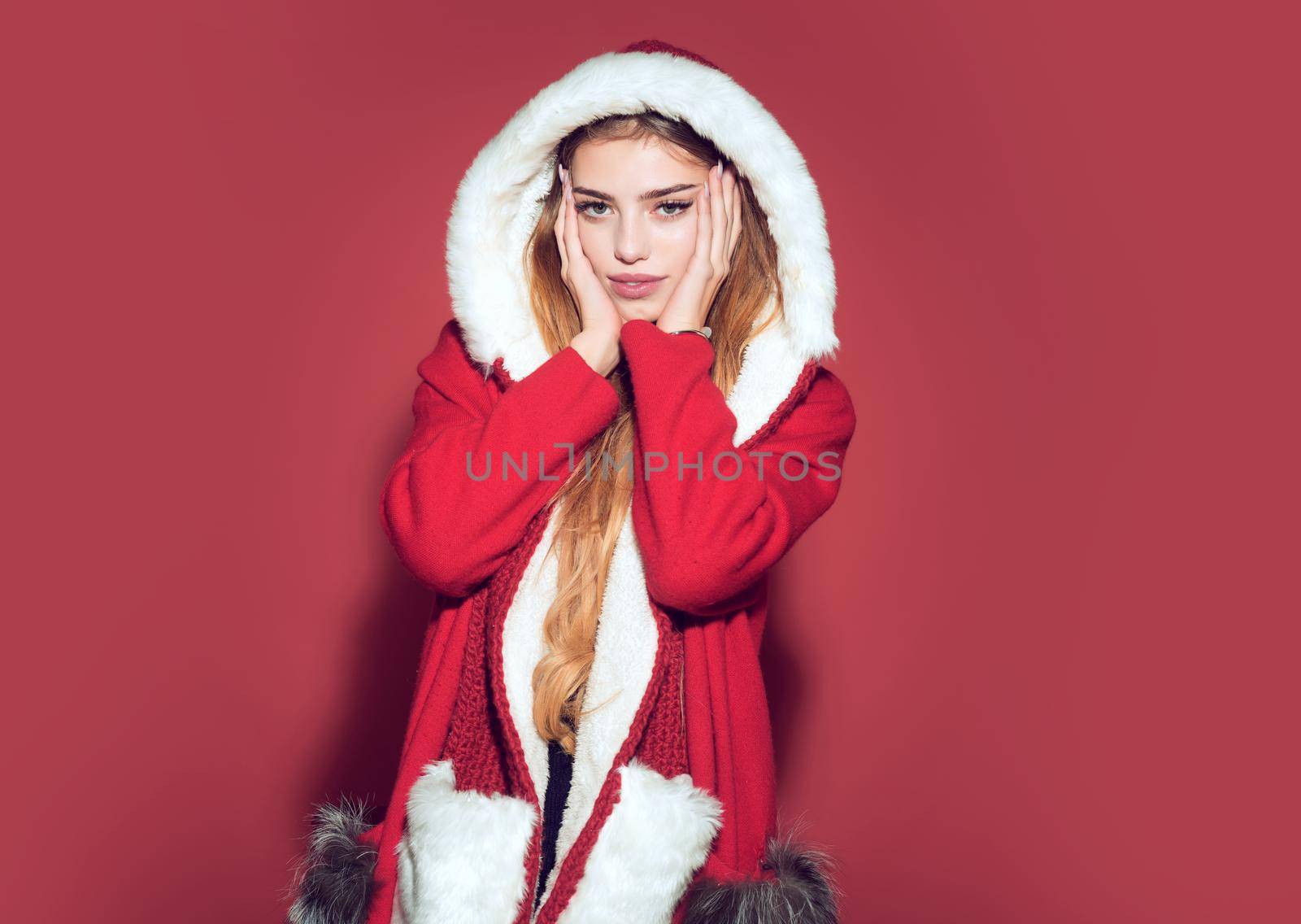 Christmas woman in red hat. Happy girl celebrate new year on red background. Xmas party and winter holiday. Woman in santa costume with pretty face by Tverdokhlib