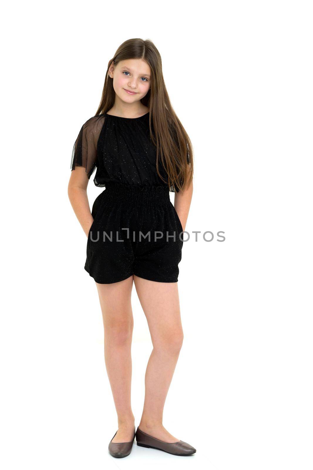 Pin-up girl in full growth smiling at the camera. Cheerful long-haired teenage girl, dressed in black overalls and shoes, stands on a white background in the studio and looks into the camera
