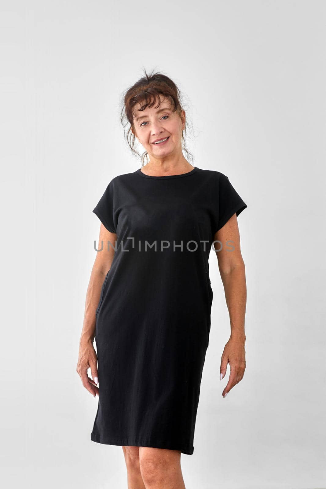 Smiling mature female model in casual black dress looking at camera against white background