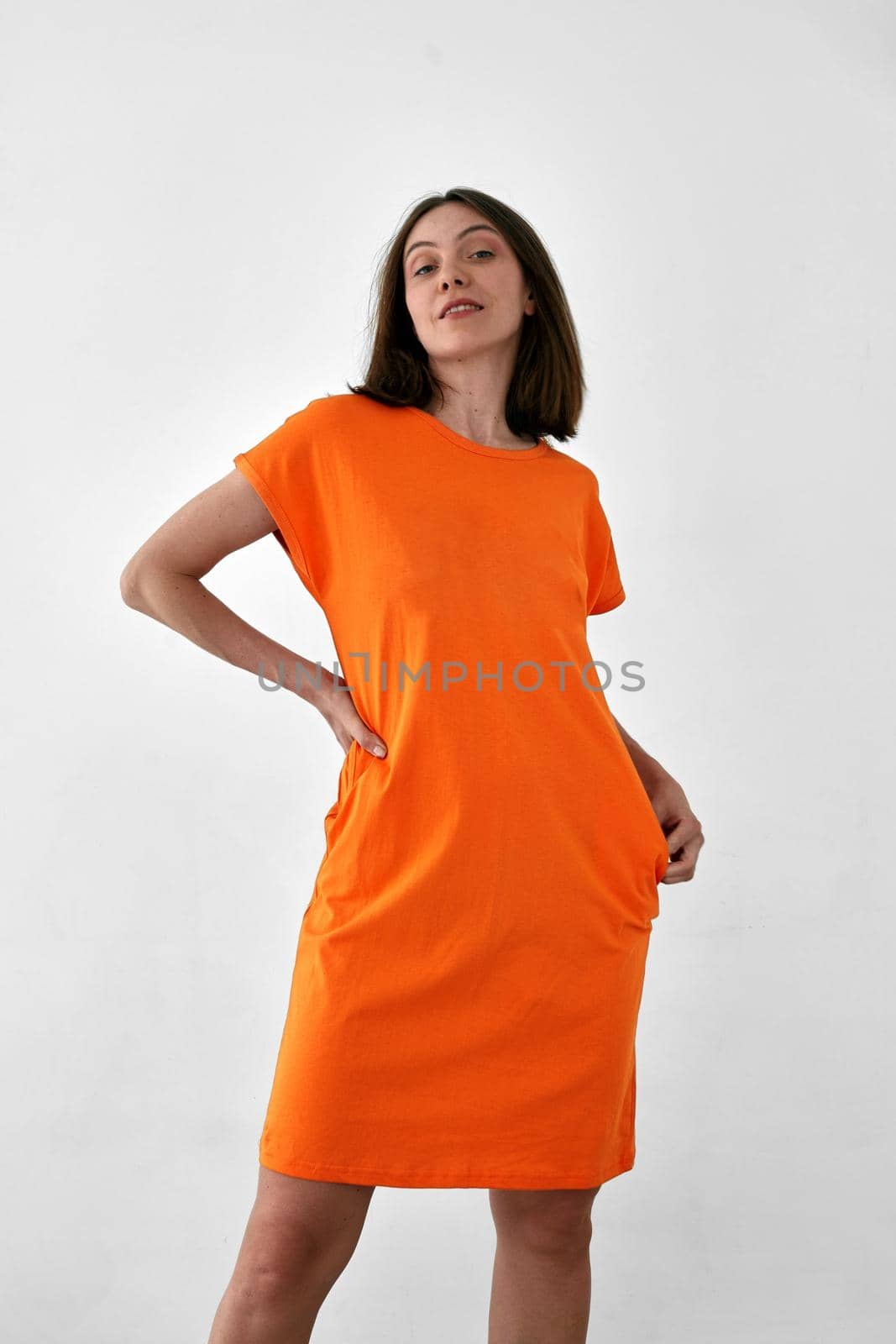 Cute female model in casual orange dress looking at camera against white background