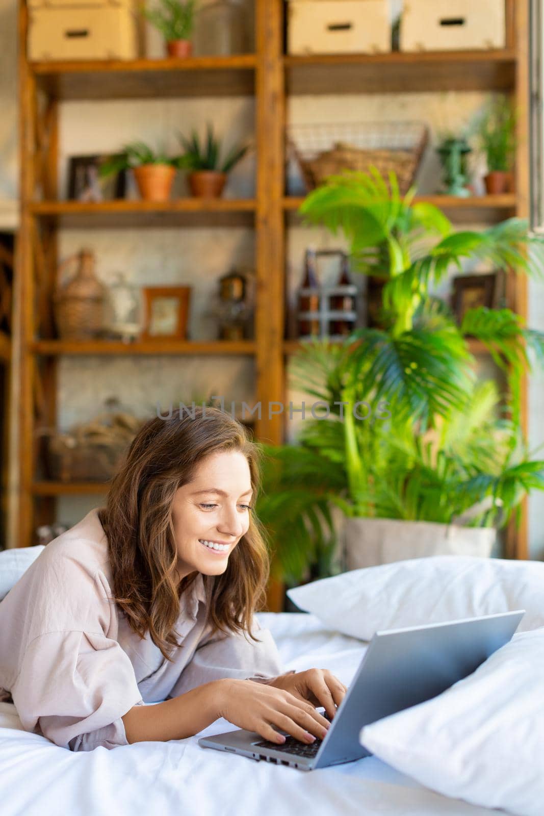 35 years old woman in front of a laptop monitor in bed. Freelance - she having online chat. Modern technology concept. Vertical photo.