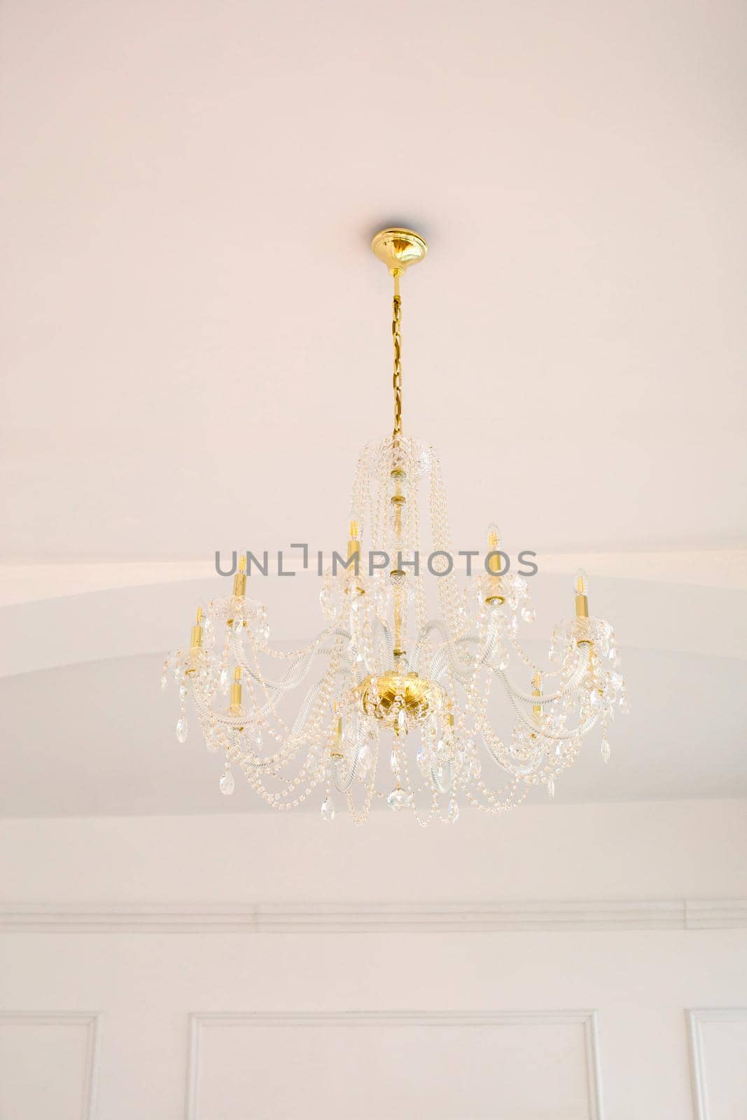 From below of classic elegant golden chandelier with crystal pendants hanging on white ceiling in light room